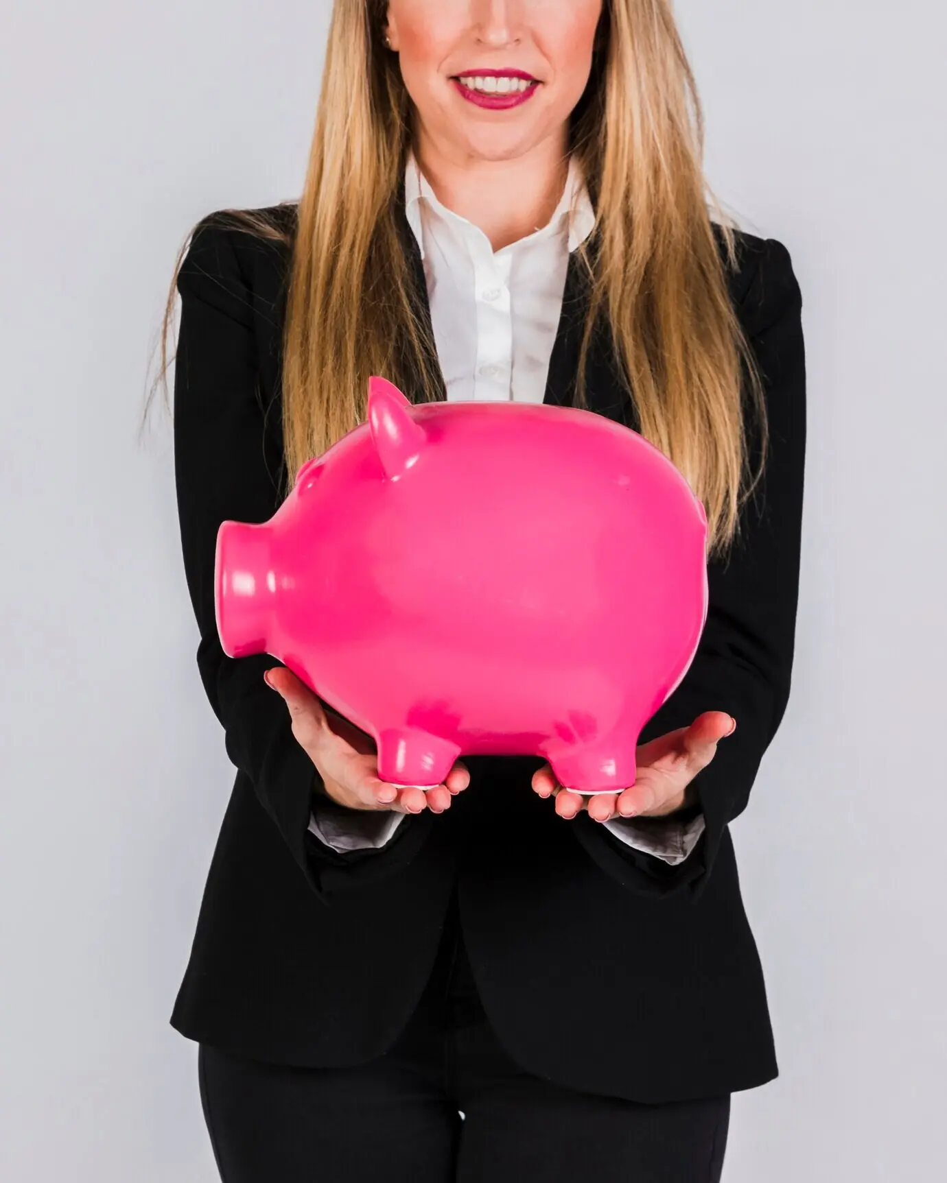Primer plano de una joven mujer de negocios sonriente que sostiene una hucha de cerámica rosa en la mano.